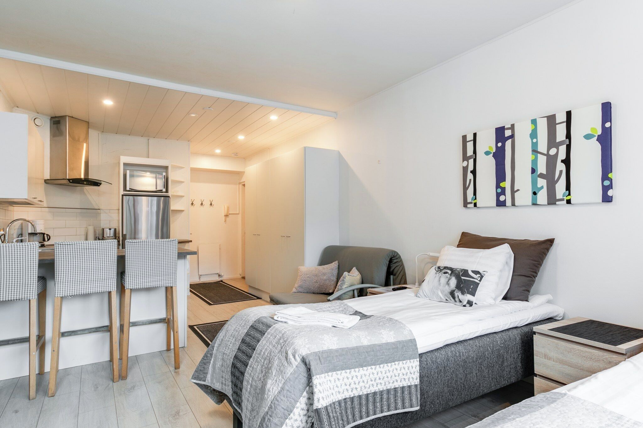 Un dormitorio moderno con cama, mesitas de noche y vistas a la cocina contigua.