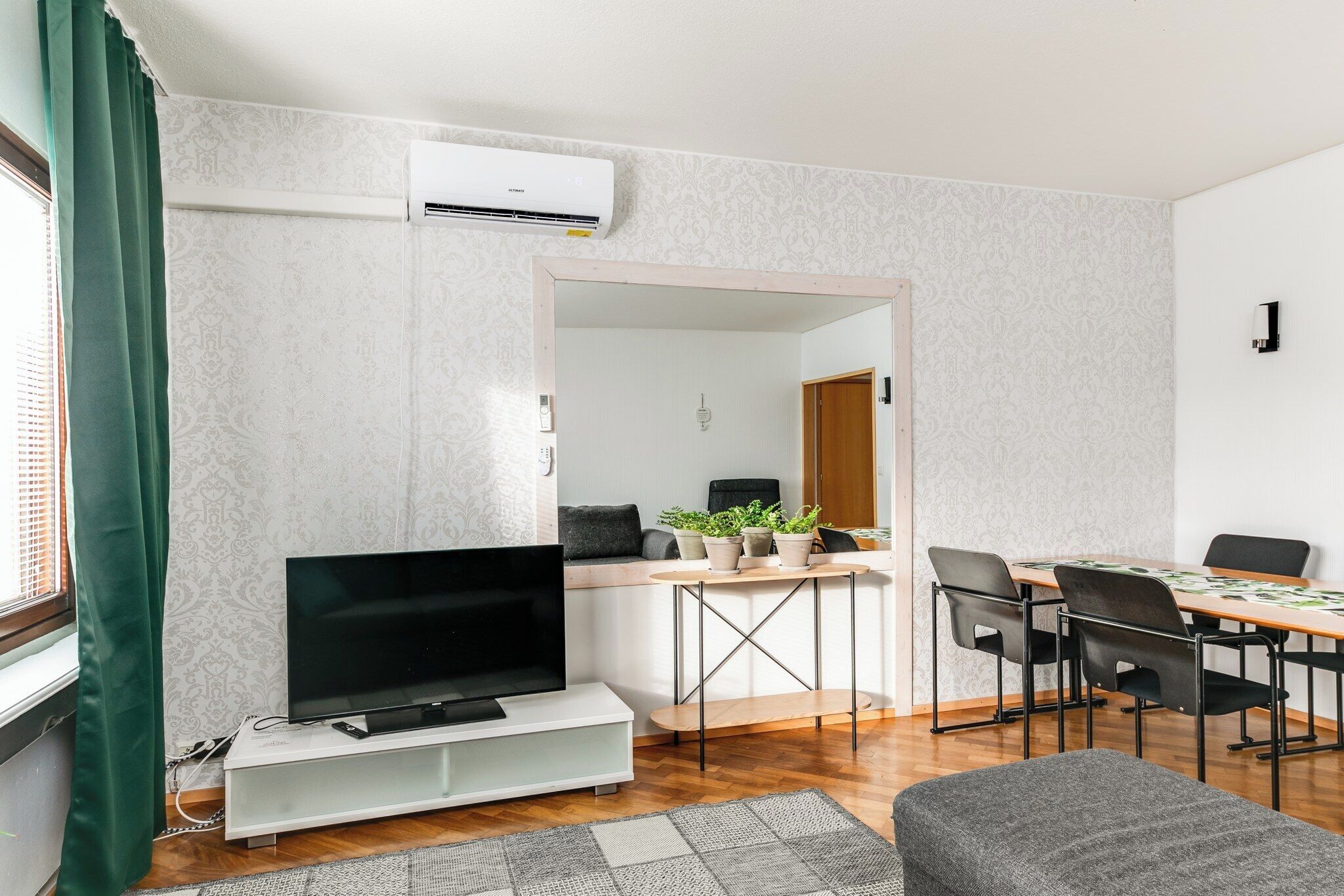 Ein Wohnzimmer mit Fernseher, Esstisch, Stühlen und einer kleinen Pflanzengruppe.