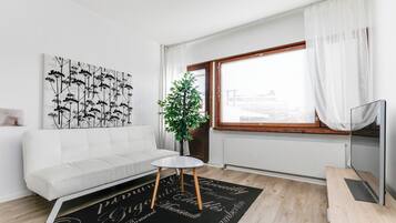 A modern living room with a white sofa, a round coffee table, a black rug with cursive writing, a potted plant, and a TV on a wooden stand.