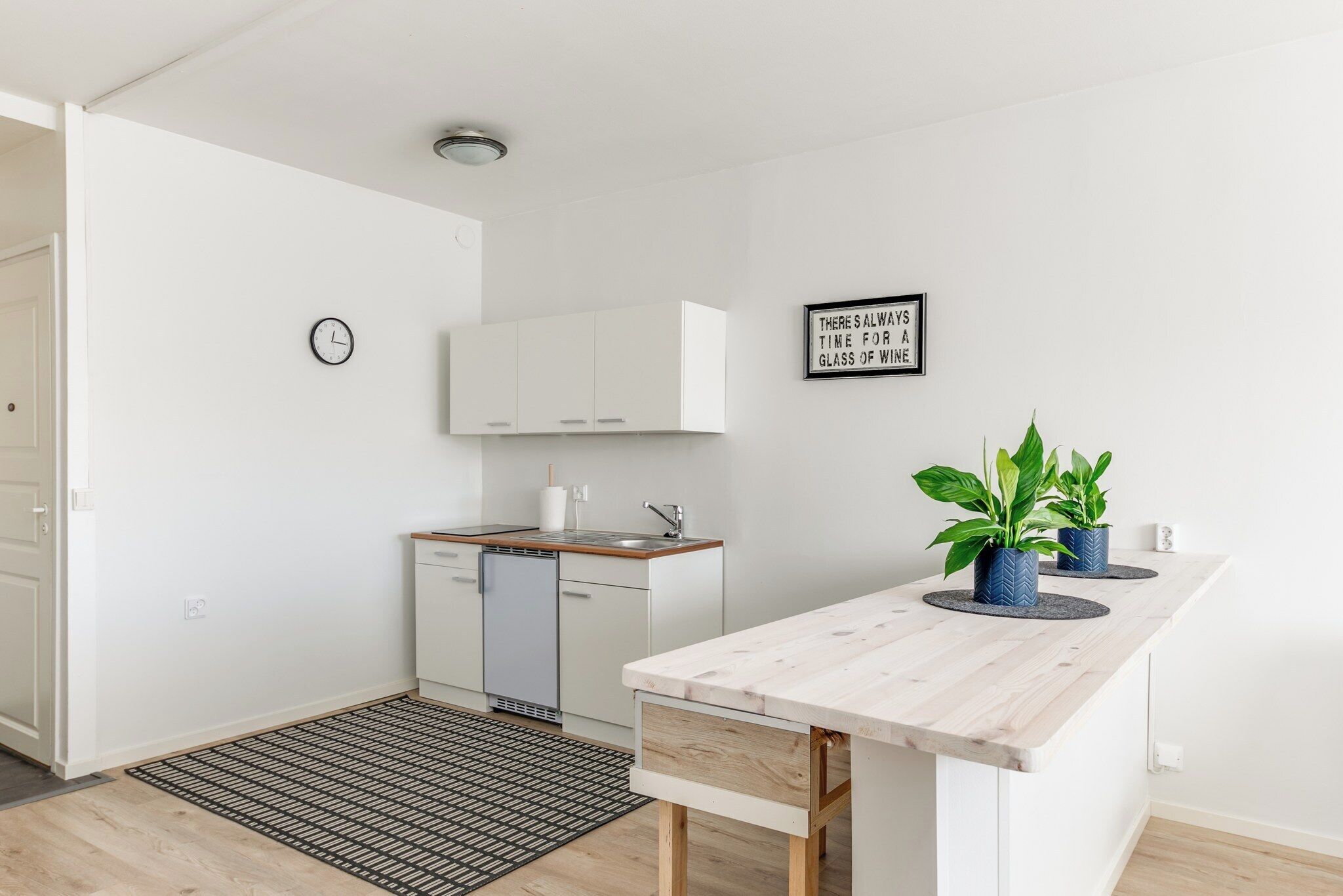 A modern kitchen with white cabinetry, a wooden countertop, and a black and white patterned rug.
