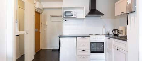 Uma cozinha compacta com armários brancos, micro-ondas, fogão e geladeira.