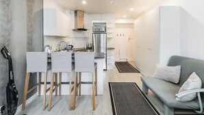 A compact kitchen with a built-in oven, a sink, and a coffee machine. There are two bar stools and a sofa with cushions. - Santa's Holiday Homes (Rovaniemi)