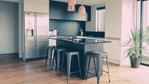 A modern kitchen with a central island, bar stools, pendant lights, and a refrigerator. - Relax In True New Modern Style (Christchurch)