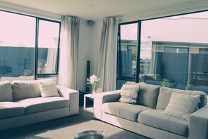Ein modernes Wohnzimmer mit zwei Sofas und einem Couchtisch, großen Fenstern und Blick auf den Garten.