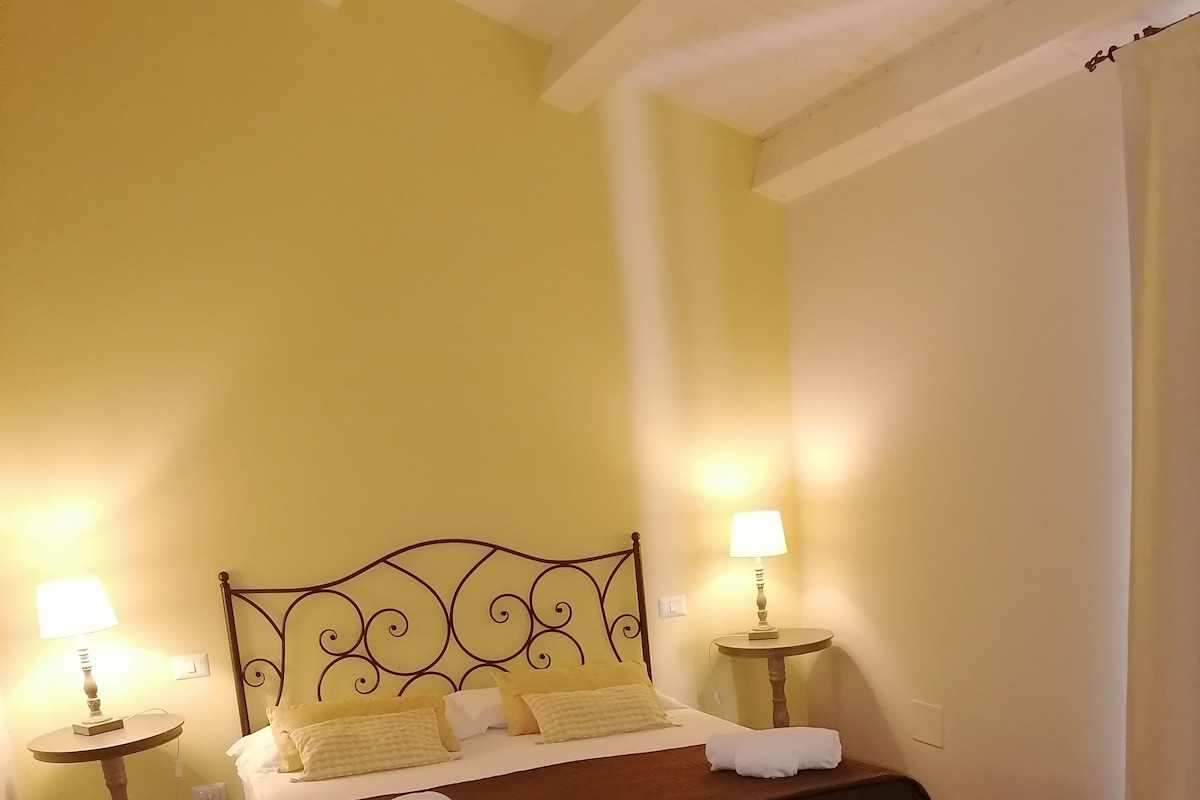 Un dormitorio con una cama, dos mesitas de noche con lámparas, un banco y una alfombra colorida.