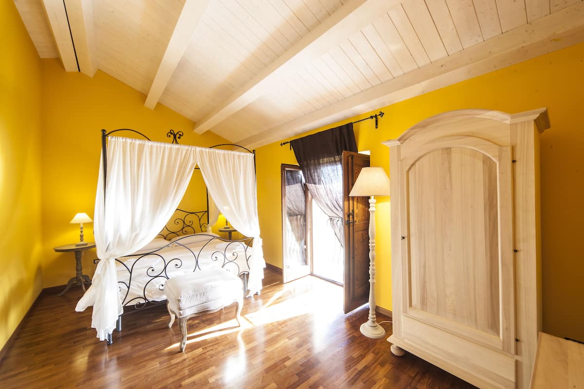 A bedroom with a bed under a canopy, a wooden wardrobe, and a nightstand with a lamp.