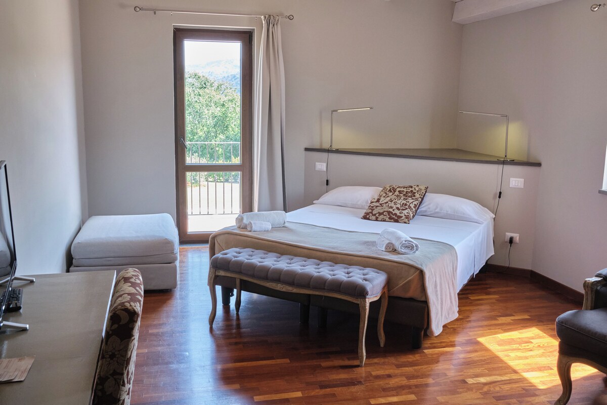 A bedroom with a bed, bench, bedside table, and a desk with a chair.