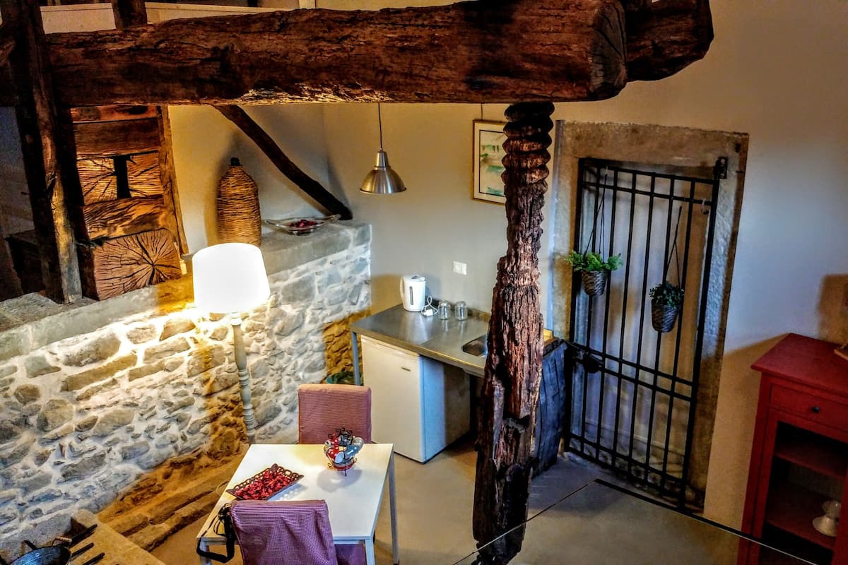 A rustic kitchen with stone walls, a wooden beam ceiling, a hanging light, and a red cabinet.