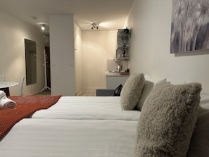 A hotel room with a bed, a small table with a chair, a kitchenette, and a bathroom. - Santa's City Apartments (Rovaniemi)