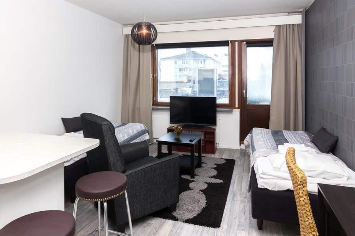 Ein Hotelzimmer mit Bett, Sofa, Fernseher, kleinem Tisch und Fenster mit Blick auf Gebäude.