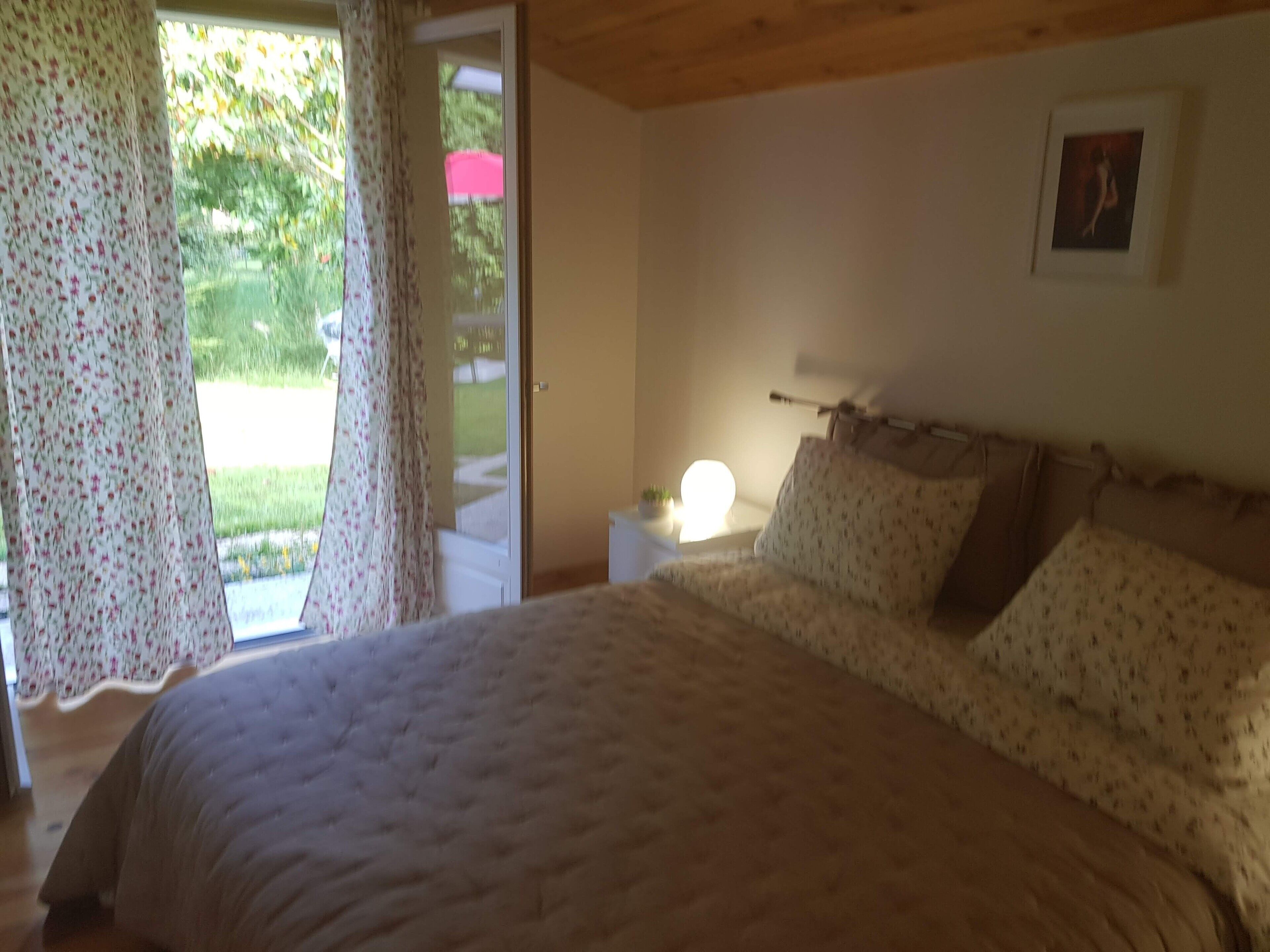 Un dormitorio con cama, mesita de noche, lámpara y ventana con cortinas.