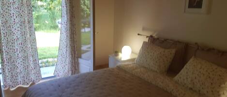 Un dormitorio con cama, mesita de noche, lámpara y ventana con cortinas.