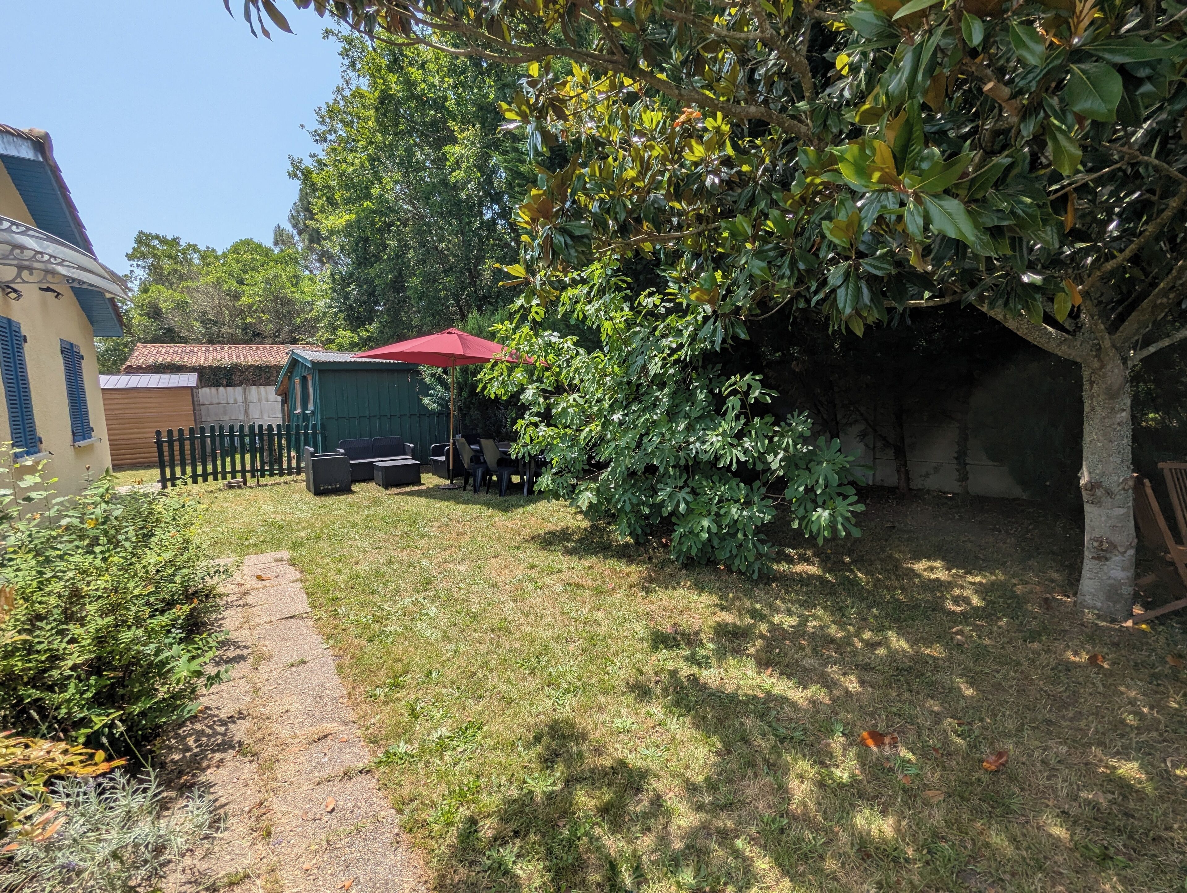 Un jardin avec une terrasse, du mobilier d’extérieur et un parasol rouge.