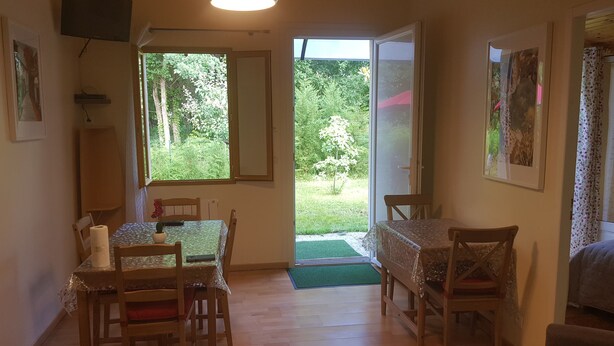 A dining area with wooden chairs and a table, a television mounted on the wall, and a view of a garden through a sliding glass door. - House between Lake and Ocean (Lacanau)