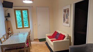 A room with a dining table, chairs, a sofa with red cushions, a grey armchair, a painting on the wall, and a window with a view of trees. - House between Lake and Ocean (Lacanau)