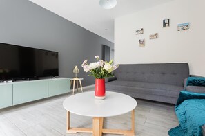 A modern living room with a flat-screen TV, a round white coffee table, a grey sofa, and a red vase with flowers. - The Waterloo Residence (London)