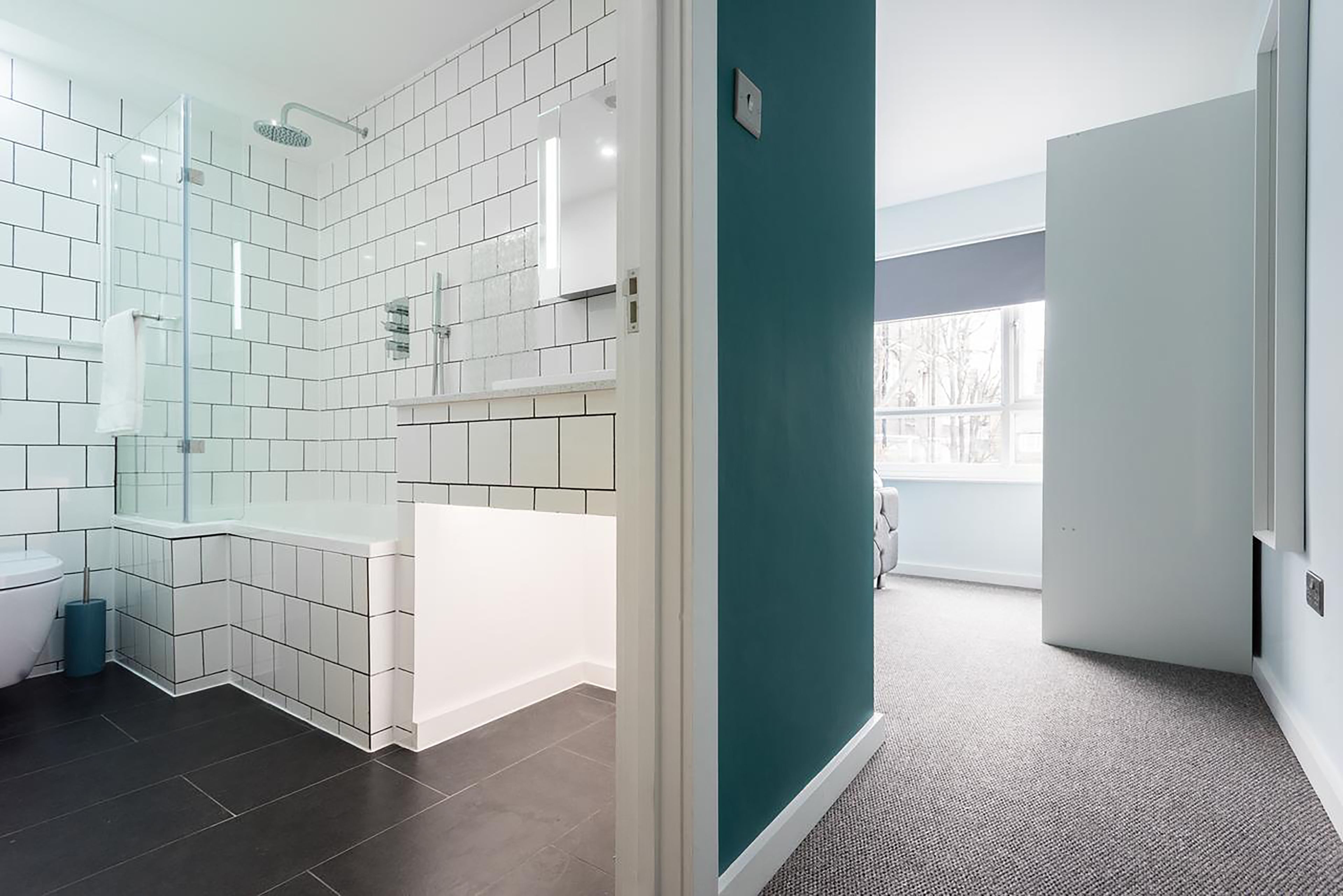 Une salle de bain moderne avec des carreaux blancs, une douche en verre et un mur d’accent de couleur turquoise.
