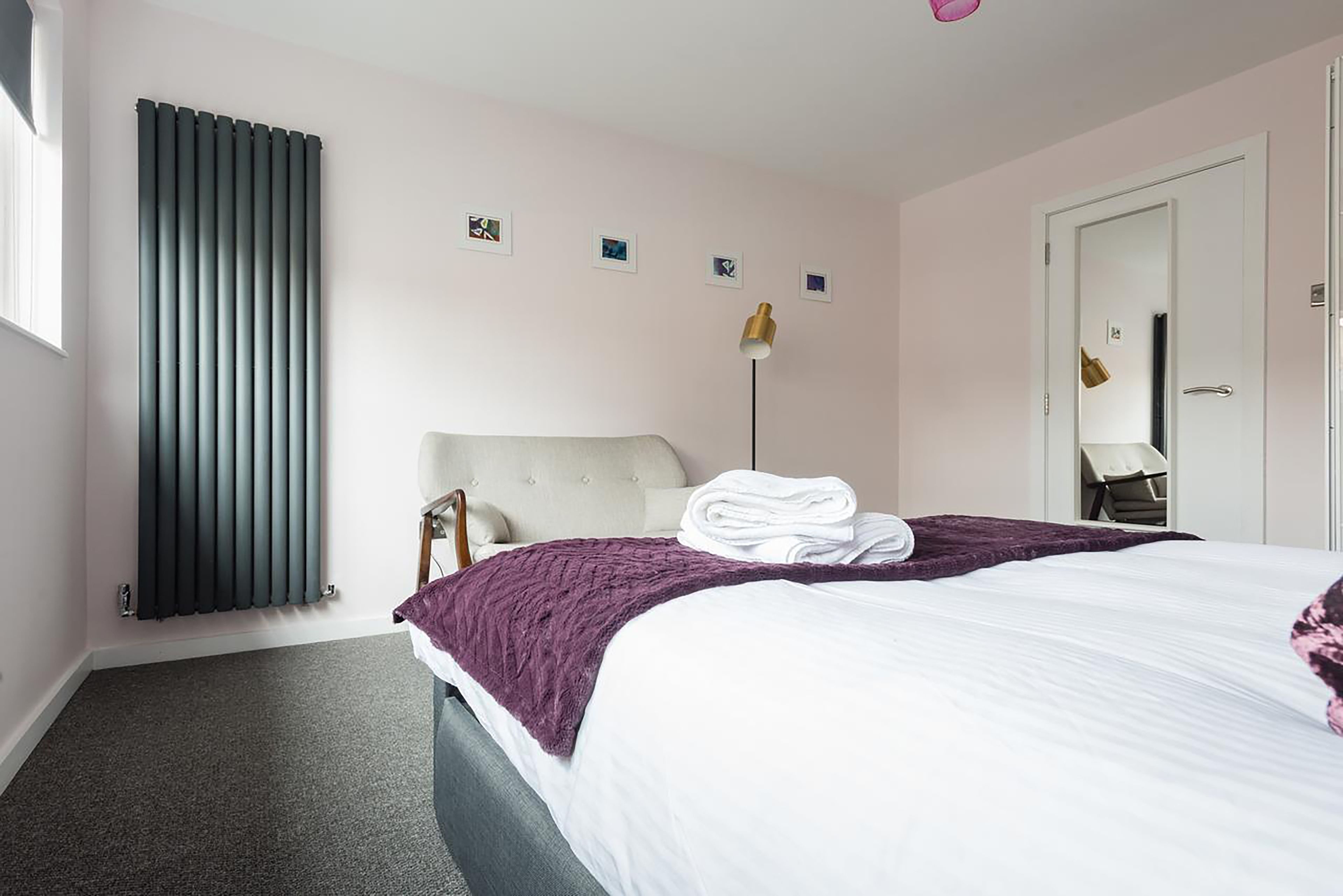 A hotel room with a bed, a radiator, a bedside table, a lamp, and a door.