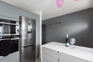 A modern kitchen with a stainless steel refrigerator, oven, and microwave. There is a white countertop with a bottle of wine and a glass. - The Waterloo Residence (London)