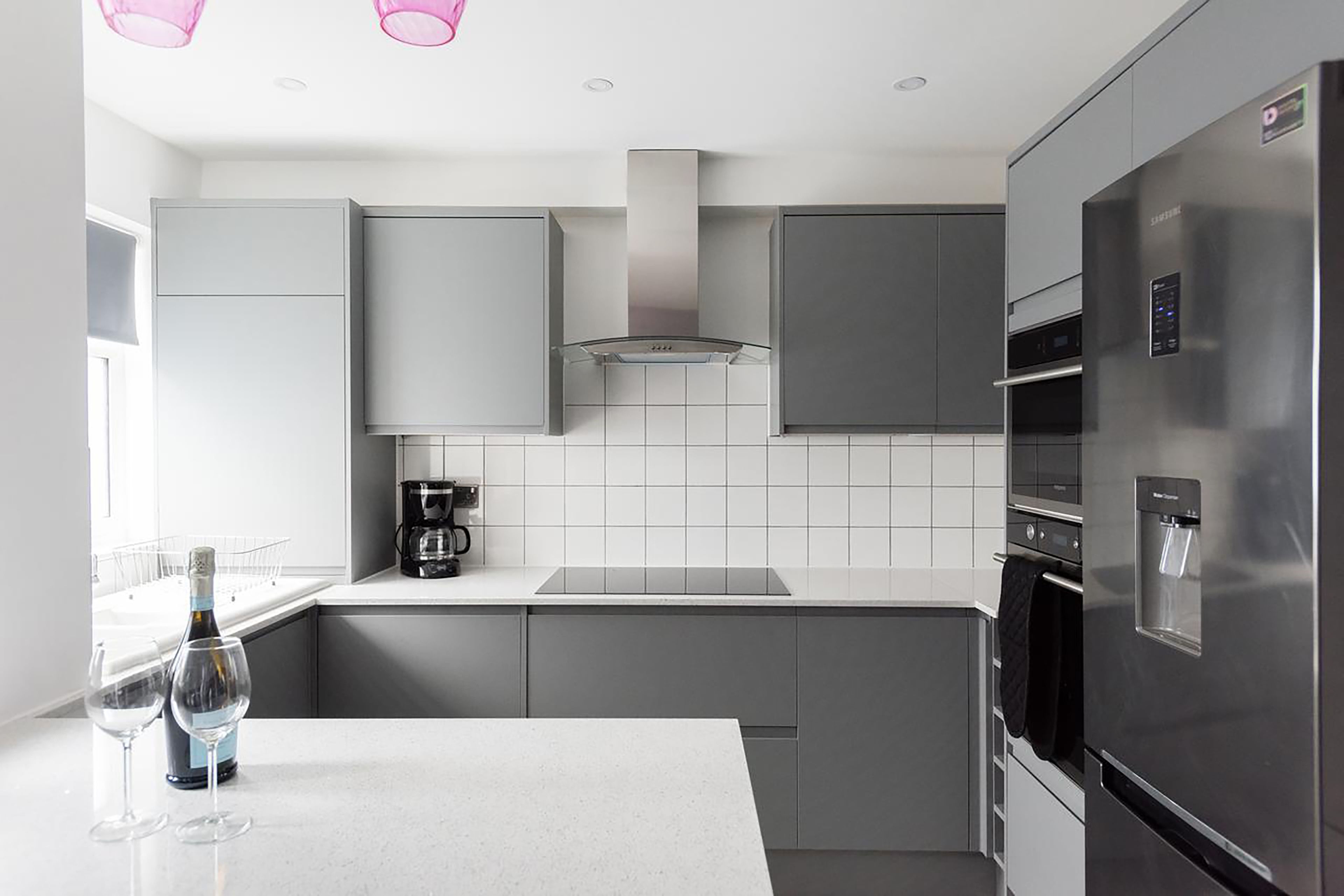 A modern kitchen with grey cabinets, a stainless steel refrigerator, and a coffee maker.