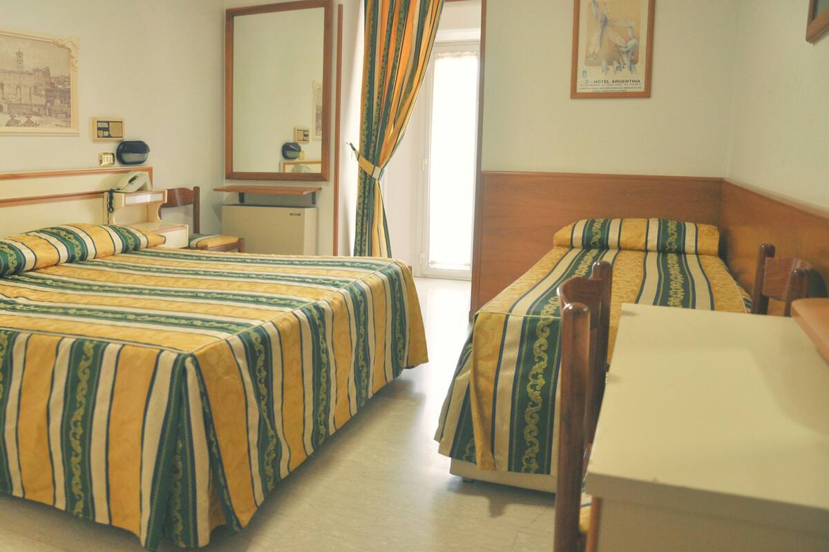 A hotel room with two beds, a desk, a chair, a mirror, and a framed picture on the wall.