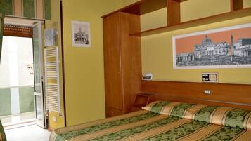 Une chambre d’hôtel avec un lit, une armoire en bois, une petite table et une étagère fixée au mur.