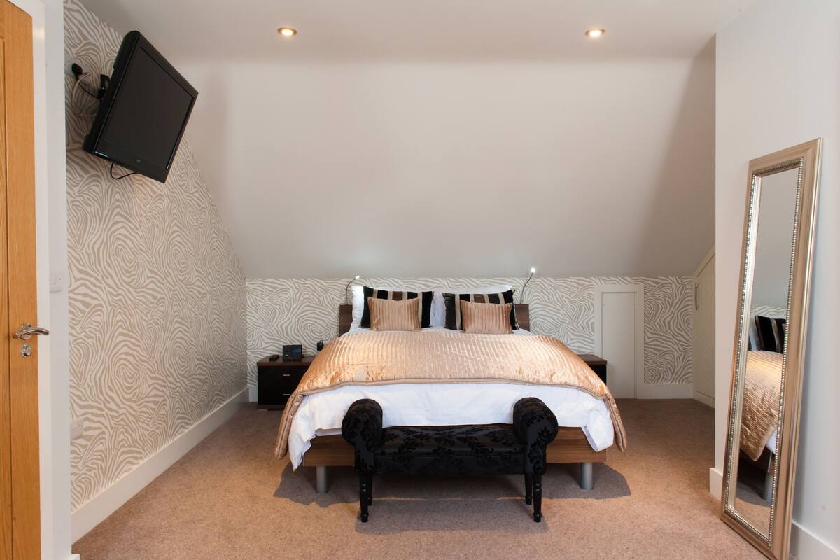 A bedroom with a bed, a bench, a nightstand, a TV mounted on the wall, and a mirror.