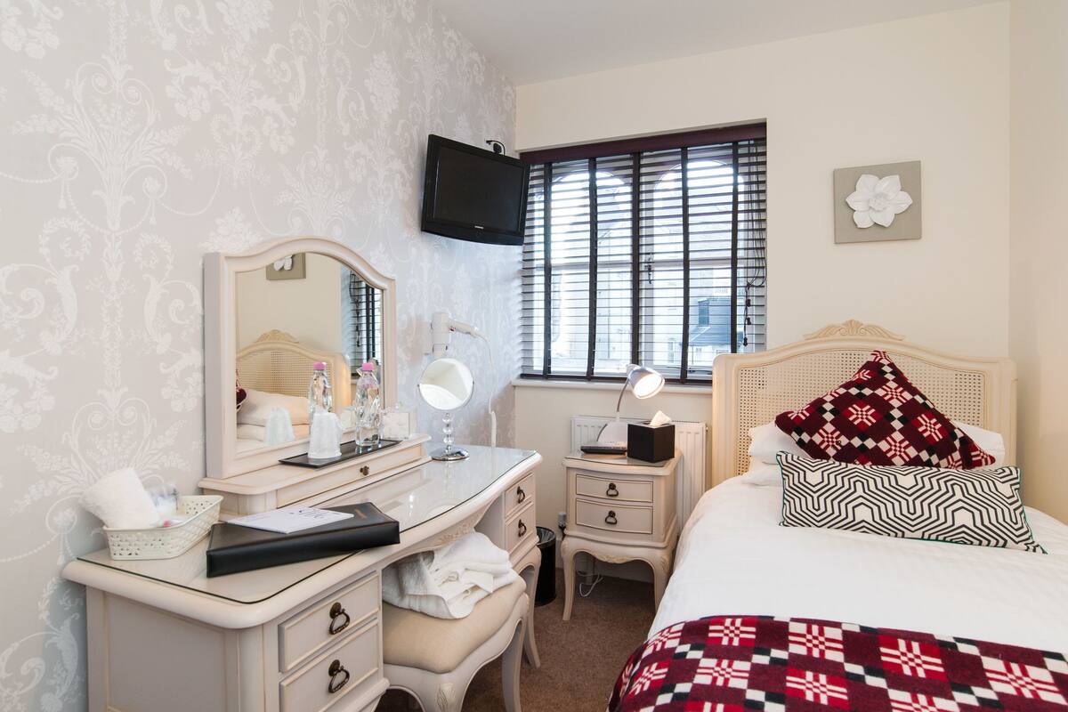 A bedroom with a vanity, bed, and a television mounted on the wall.