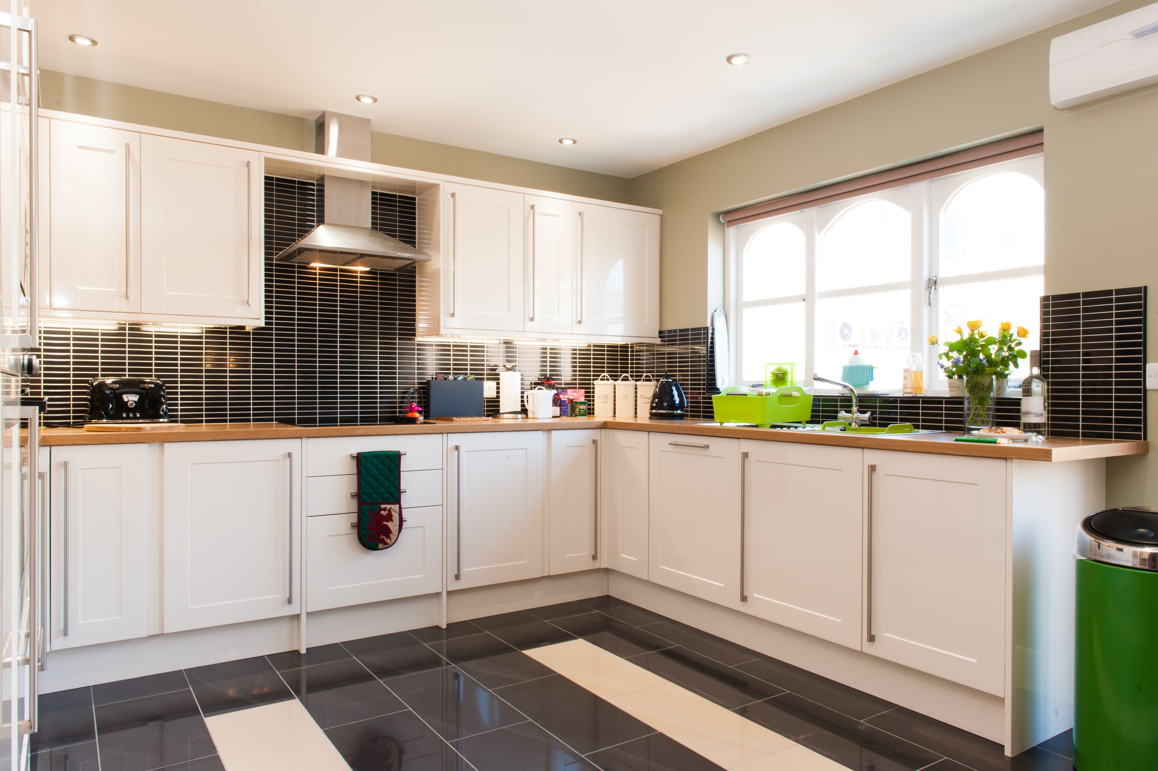 A modern kitchen with white cabinets, a black and white tiled backsplash, and a window with a view of the outdoors.