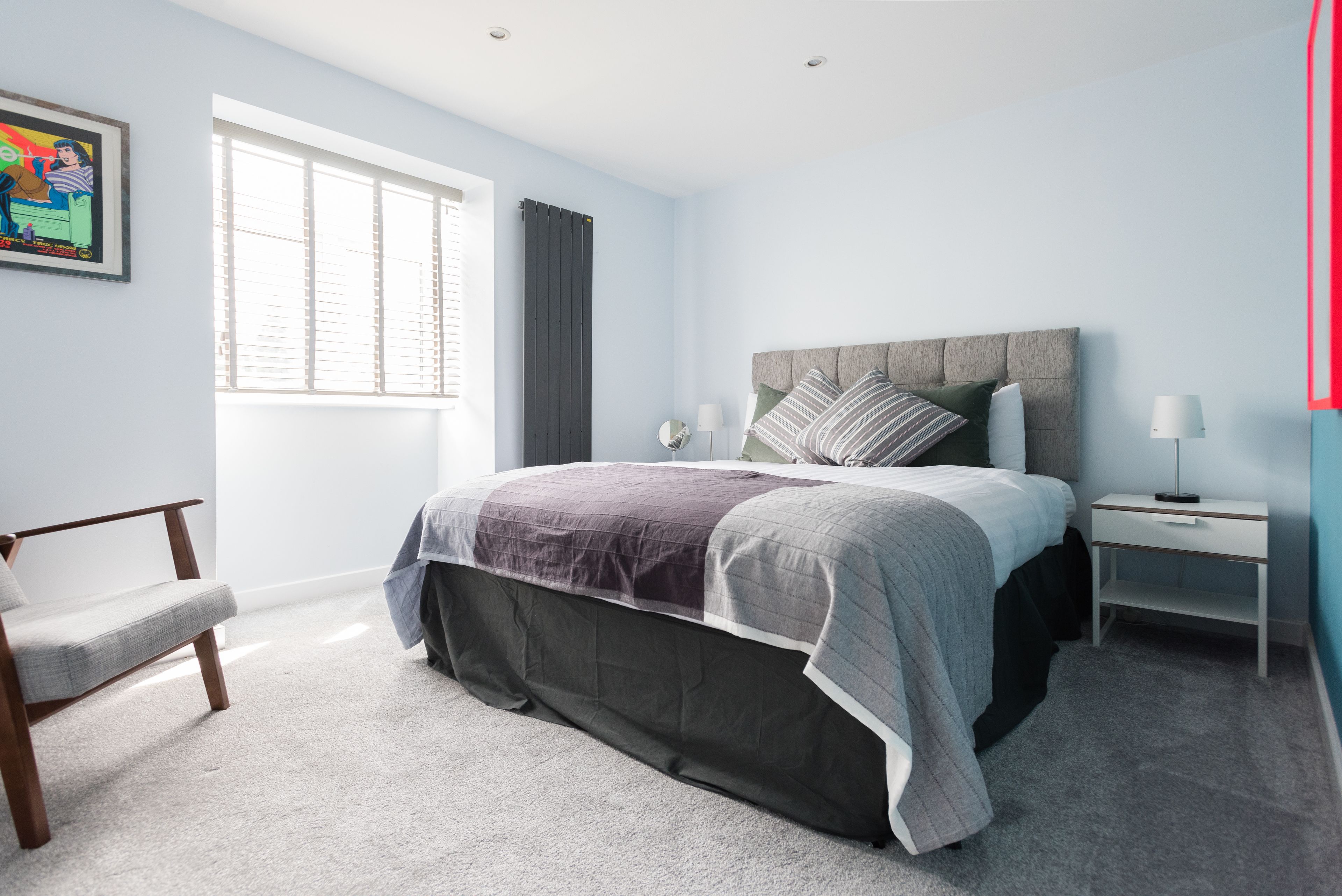 A bedroom with a bed, a chair, a bedside table, and a window.