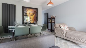 A modern living room with a dining area, featuring a sofa, dining table, chairs, pendant lights, and a large abstract painting. - The Nine Elms Residence (London)