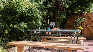 A wooden picnic table with a bottle and glasses on it, set against a backdrop of greenery and a wooden fence. - The Nine Elms Residence (London)