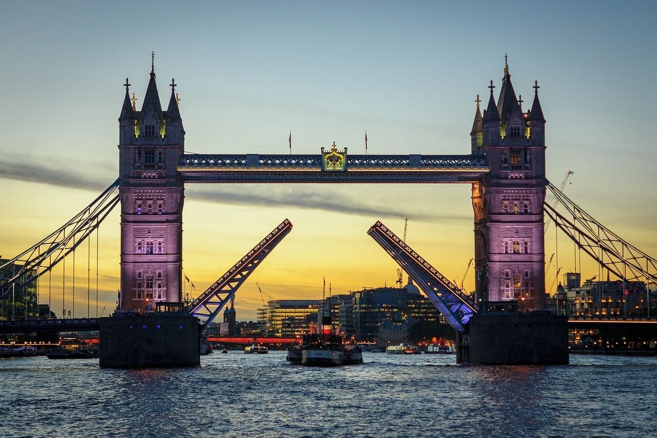 A large, illuminated bridge with two towers and a central arch, spanning a body of water with boats.