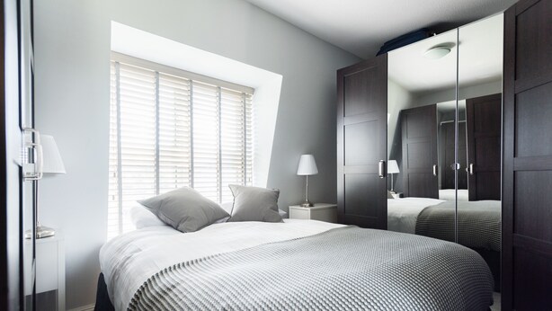A bedroom with a large bed, a nightstand, a lamp, a window with blinds, and a wardrobe with a mirror. - The Nine Elms Residence (London)