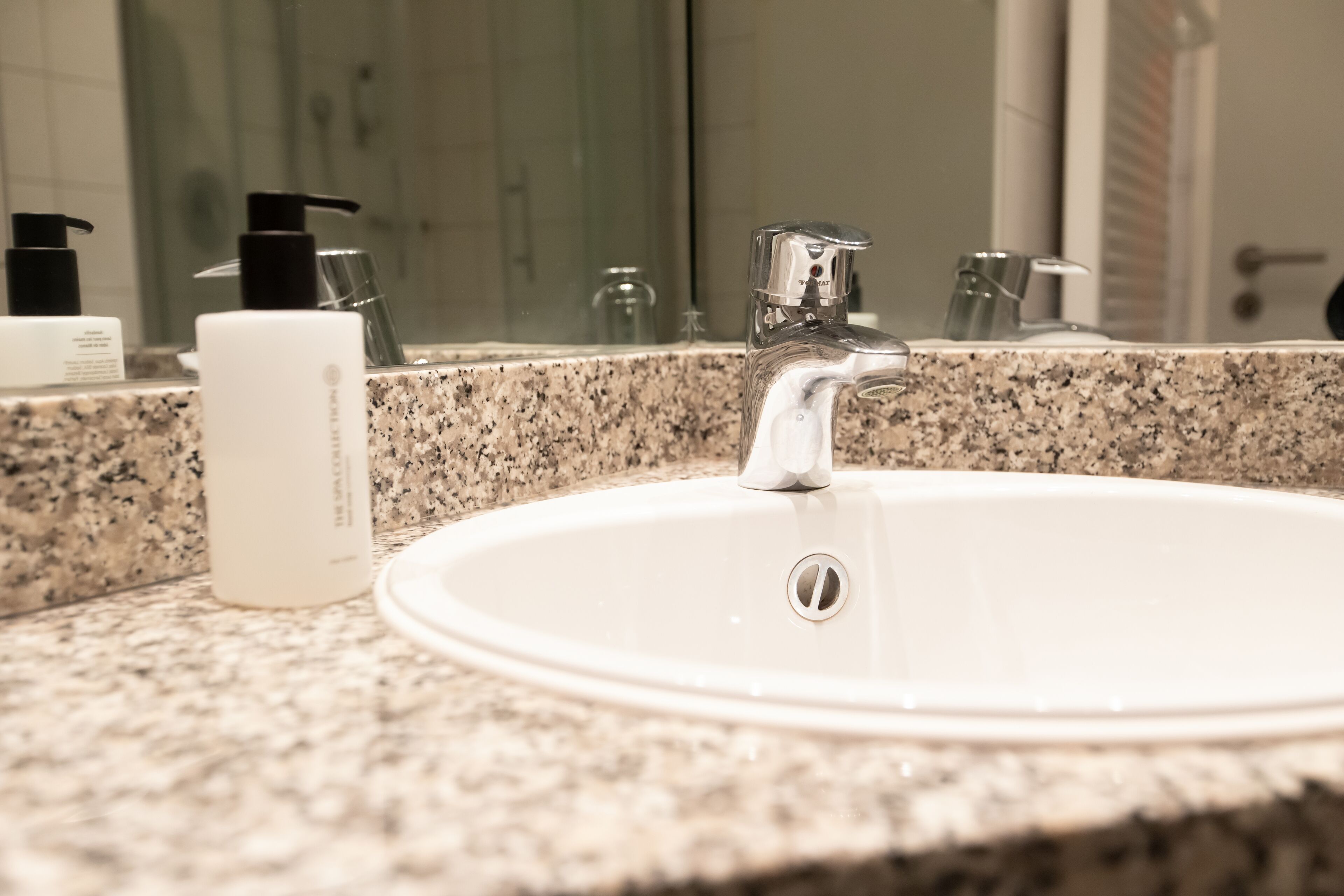 Un lavabo con encimera de granito, un espejo y artículos de aseo.