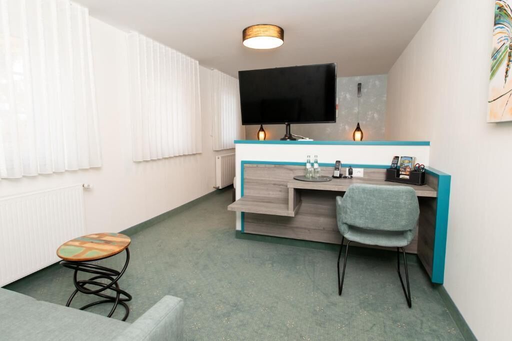 A compact hotel room with a kitchenette, a flat-screen TV, a small dining table, and a single chair.