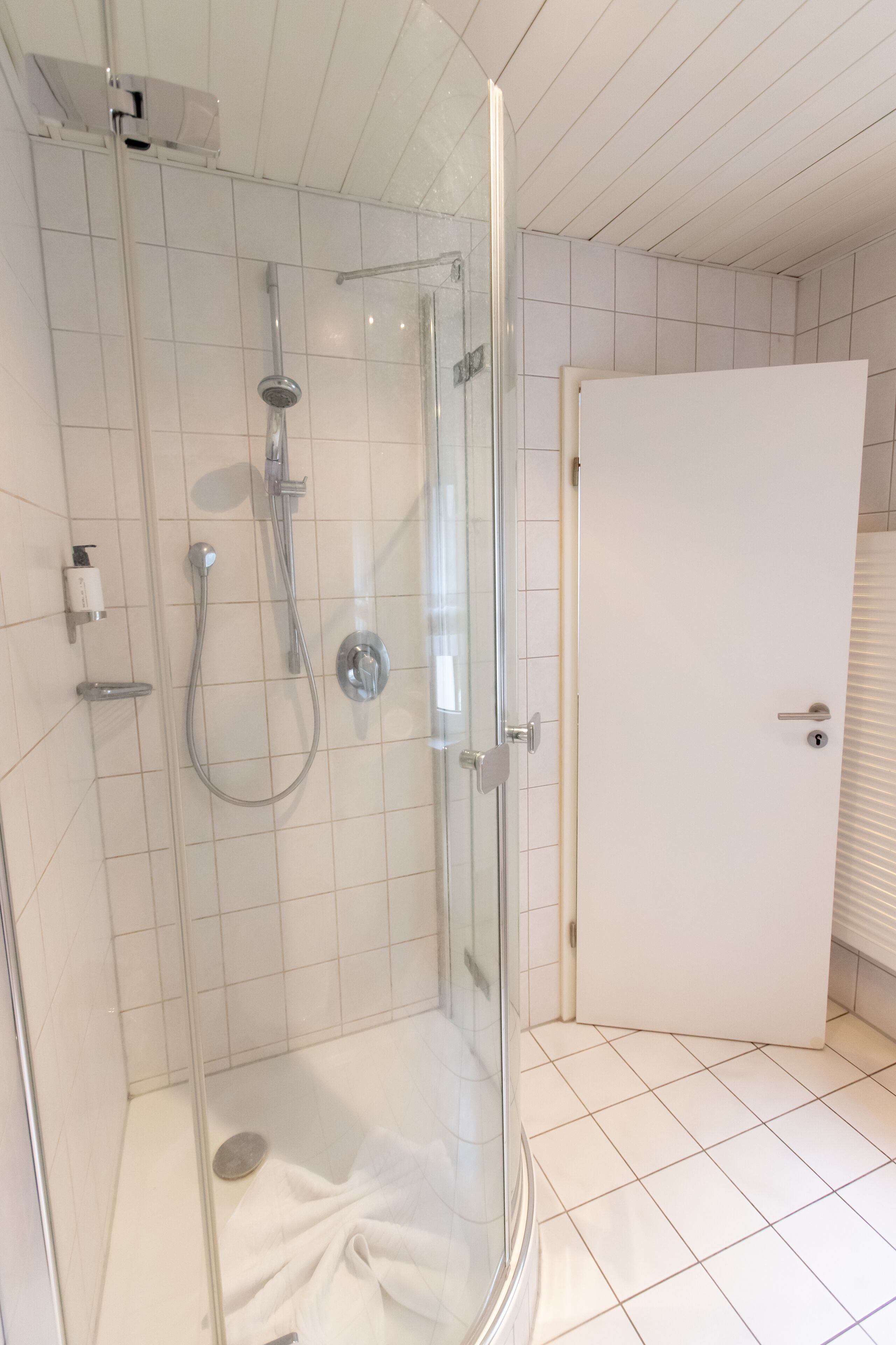 Cabina doccia in vetro con soffione a mano e rubinetto a parete.