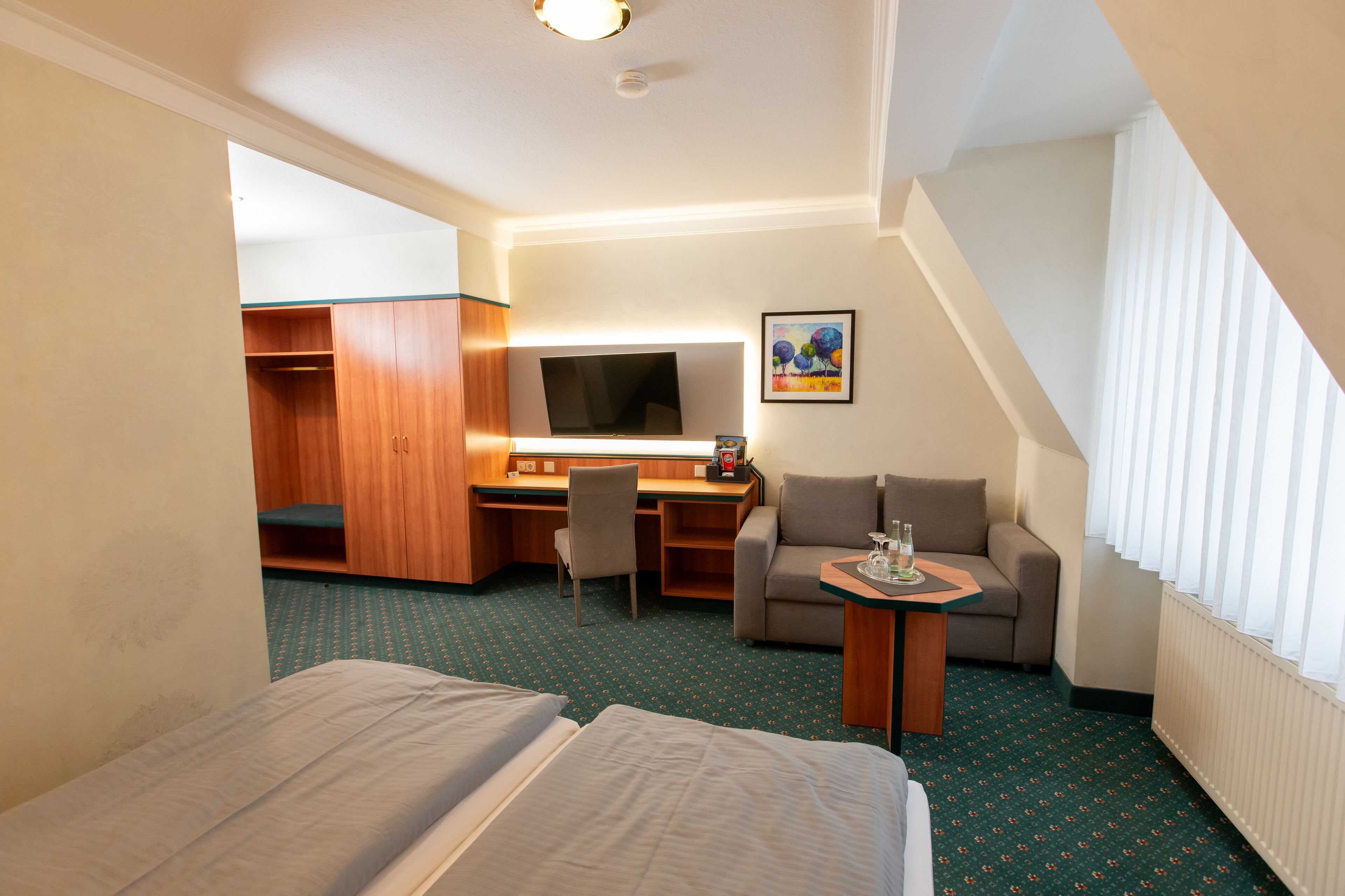 A hotel room with two beds, a desk with a chair, a sofa, and a TV.