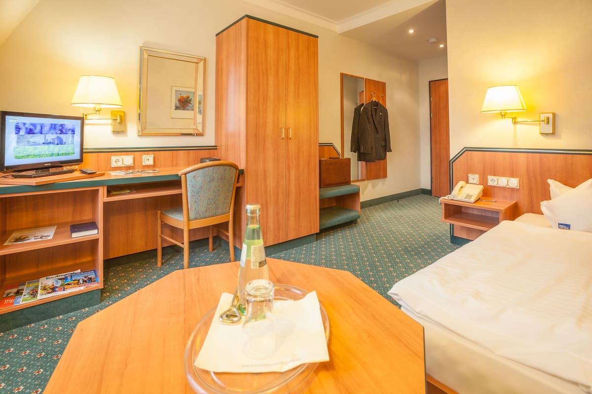 Une chambre d’hôtel comprenant un lit, un bureau avec un ordinateur, une chaise, une armoire et une table de chevet avec une lampe.