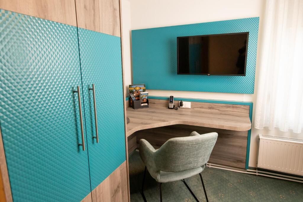 Una habitación con un armario azul aguamarina, un escritorio de madera, una silla gris y un televisor montado en la pared.