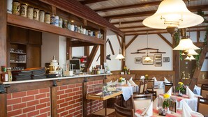 Un restaurant aux murs de briques, aux poutres apparentes et aux lampes suspendues. Les tables sont dressées avec des nappes et des serviettes blanches.