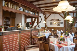 En restaurang med tegelväggar, träbjälkar och hängande lampor. Borden är dukade med vita dukar och servetter.