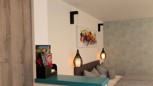 Une chambre à coucher moderne avec un mur d’accent de couleur turquoise, un canapé gris, un lit avec une literie grise, un tableau abstrait accroché au mur et un luminaire suspendu noir.