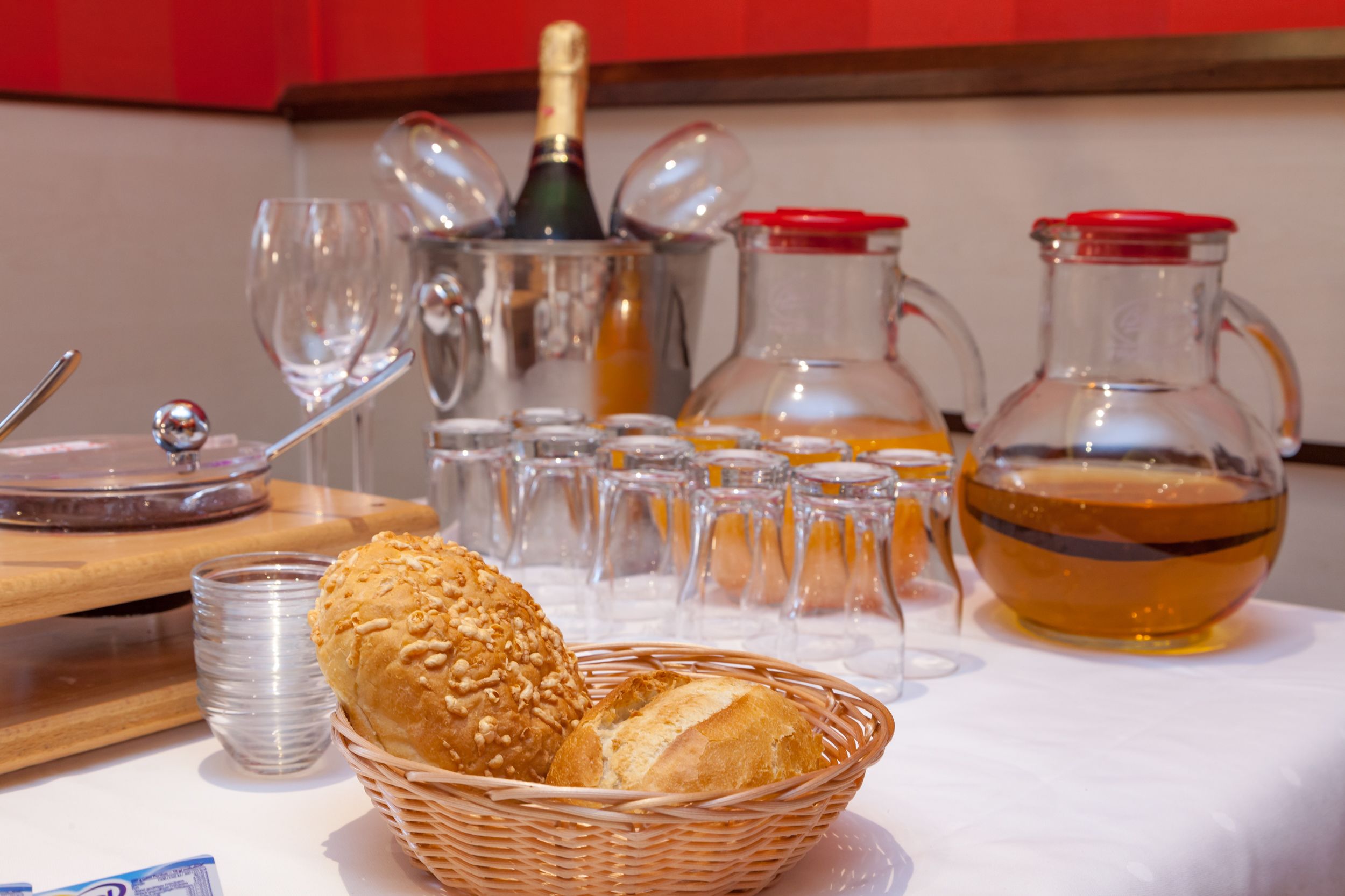 A table with a basket of bread, a bottle of champagne, and several glasses and pitchers.