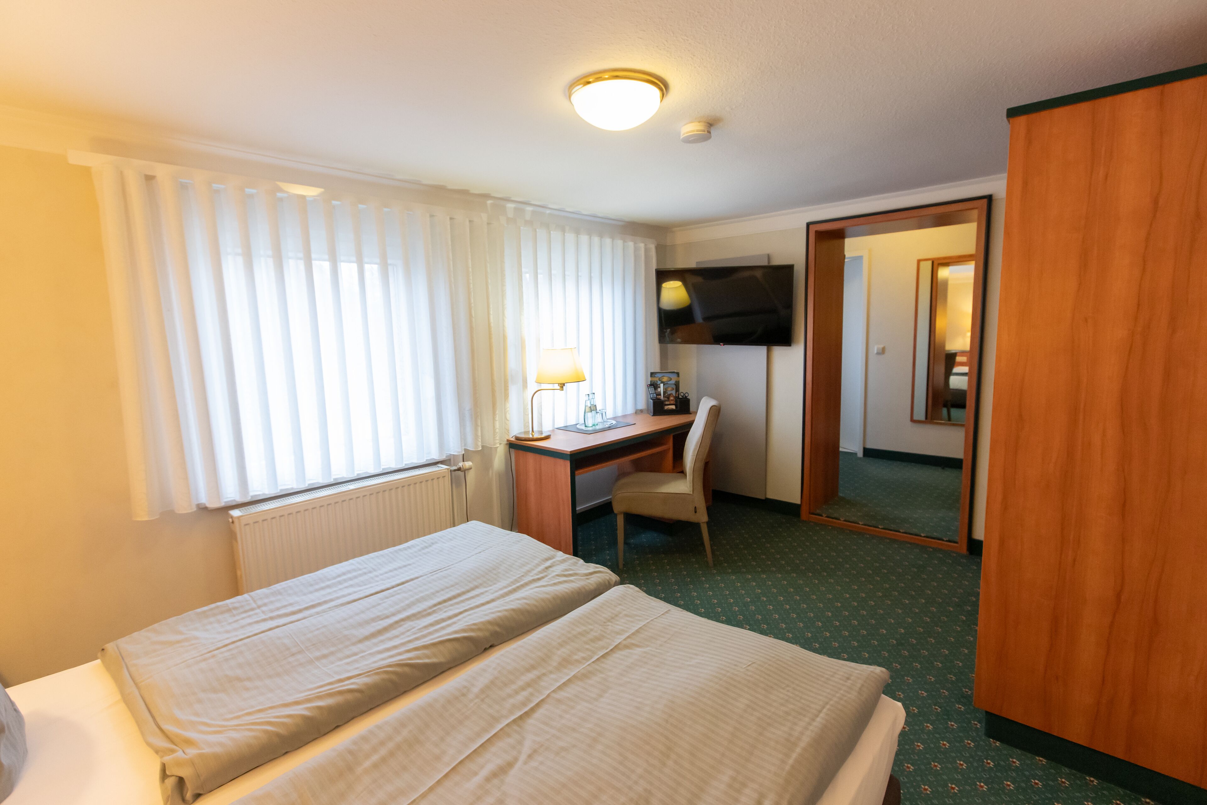 Habitación de hotel con dos camas, un escritorio con silla, televisión y espejo.