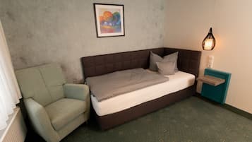 Un dormitorio con cama, una silla, una mesita de noche, una lámpara y un cuadro en la pared.
