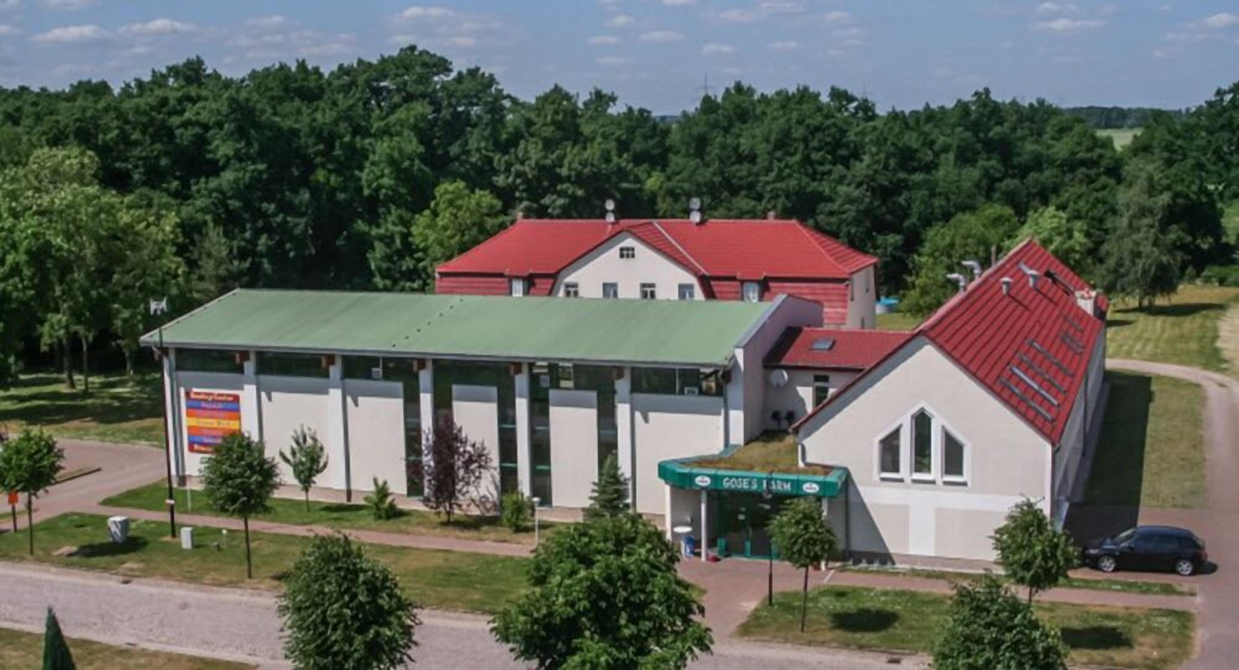 A building with a green roof and a red roof, surrounded by trees and a road.