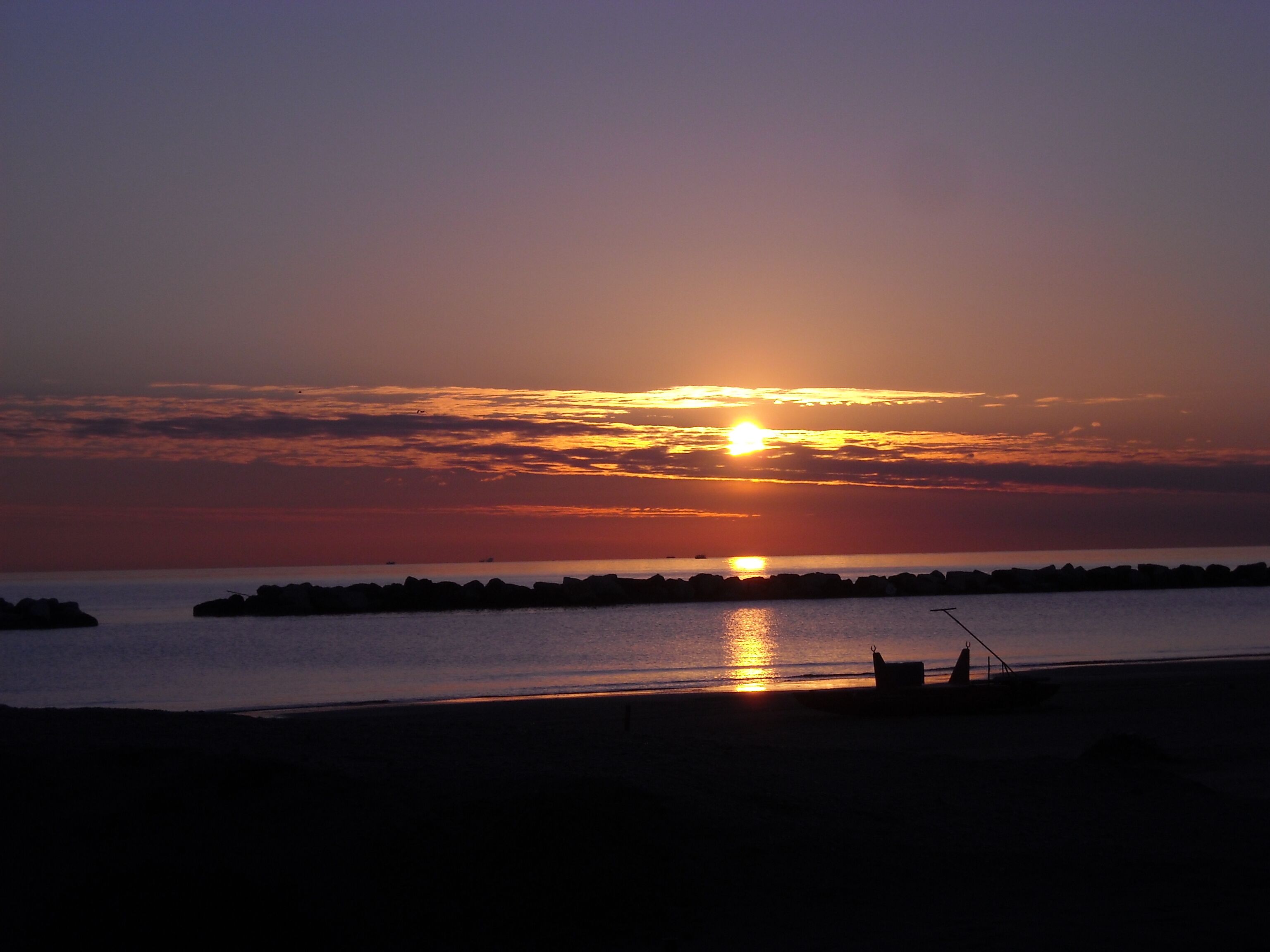 Un coucher de soleil sur une mer calme, avec une jetée et un bateau.