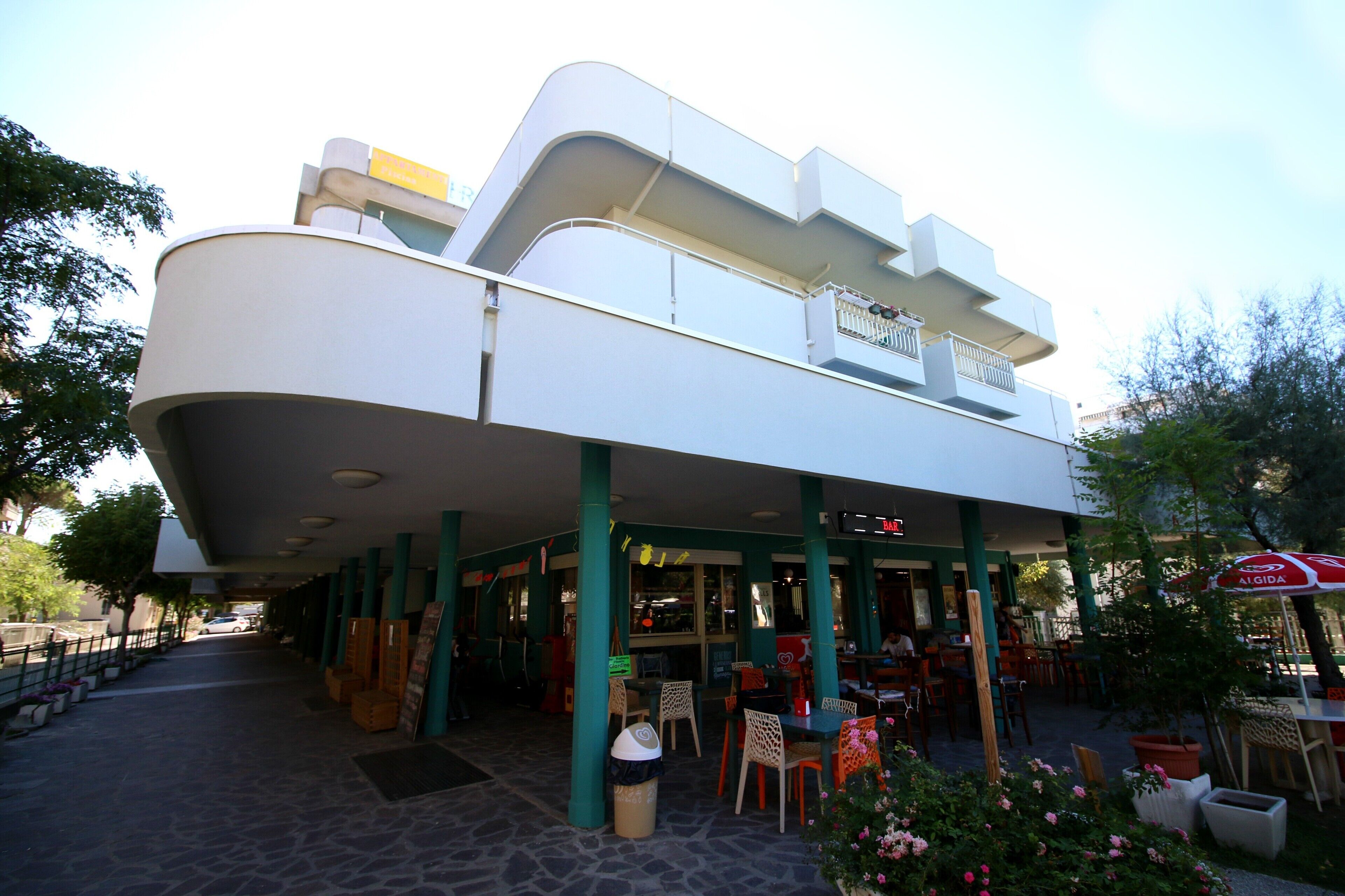 A modern building with a flat roof, a covered outdoor seating area, and a sign that reads "JUGO".