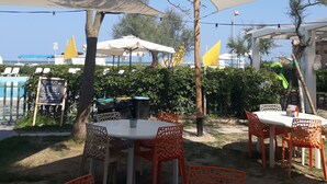 An outdoor seating area with round tables and orange chairs, shaded by large white umbrellas, overlooking a pool and greenery. - Hotel Residenza Giardino (Bellaria-Igea Marina)